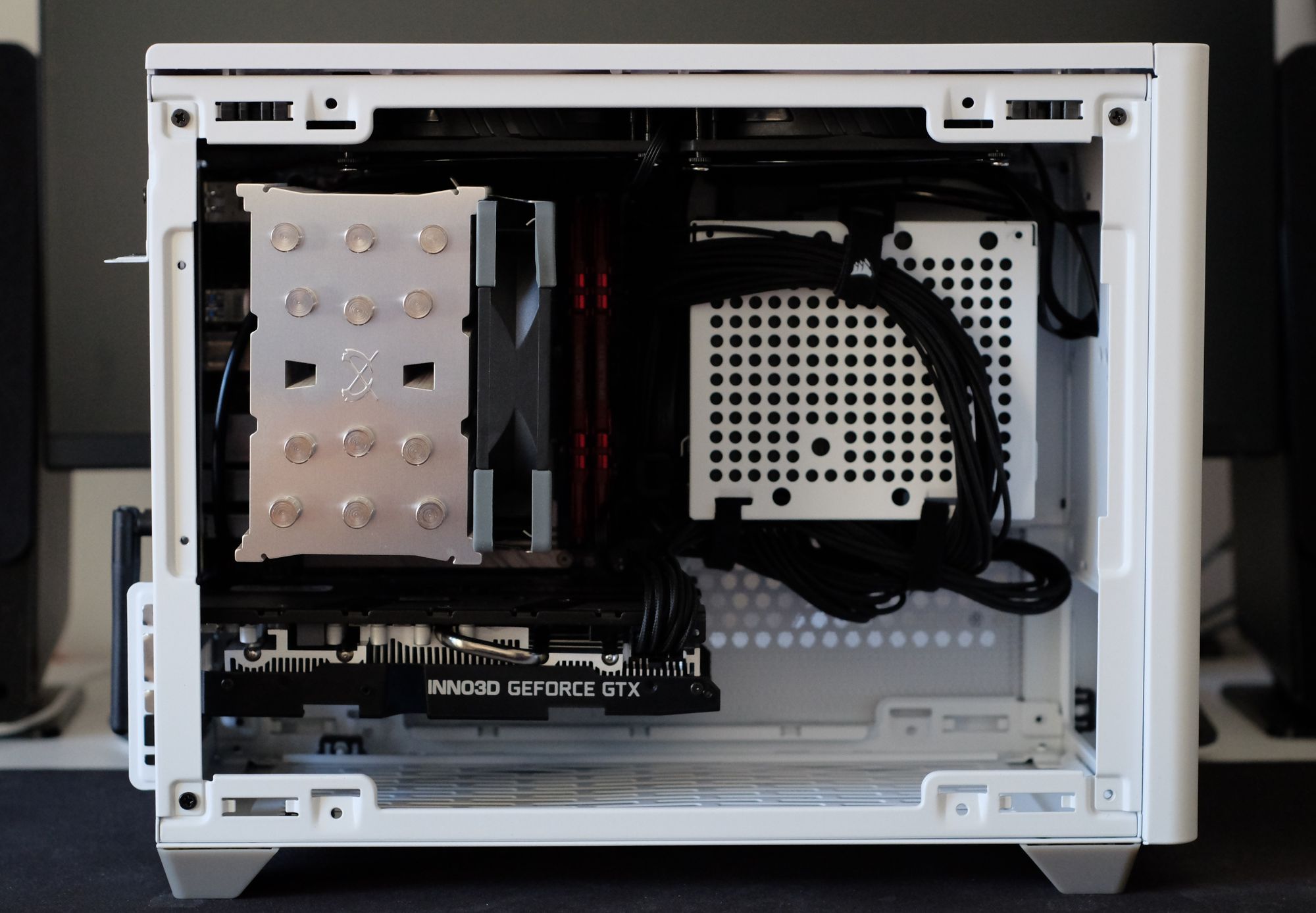 An open white computer case (CoolerMaster NR200), which shows a big CPU cooler, and a graphics card from Inno3D