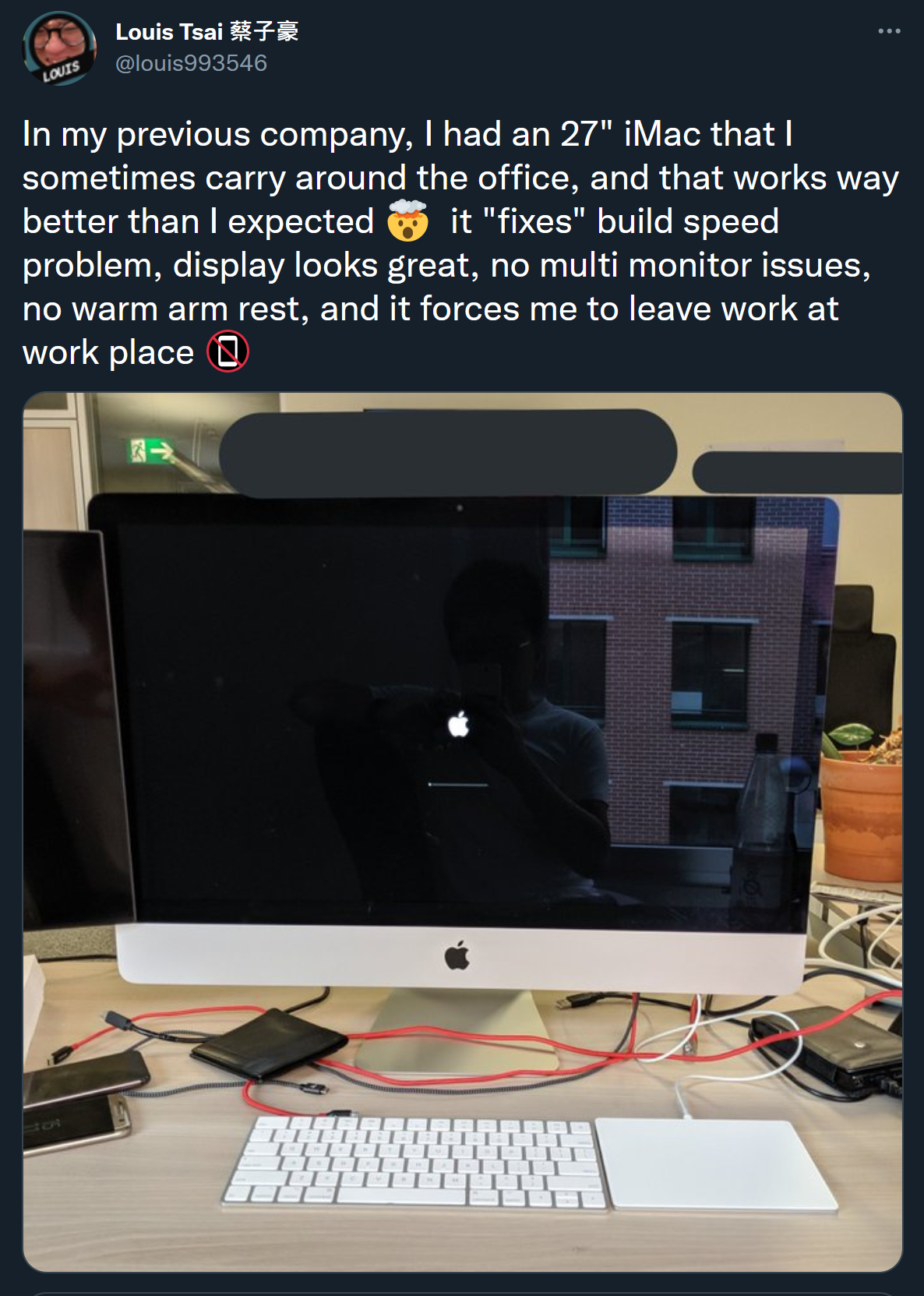 A screenshot of a Tweet from Louis (@louis993546), which has a picture of an iMac in the boot screen, on an office desk. The tweet writes "In my previous company, I had an 27" iMac that I sometimes carry around the office, and that works way better than I expected 🤯 it "fixes" build speed problem, display looks great, no multi monitor issues, no warm arm rest, and it forces me to leave work at work place 📵"