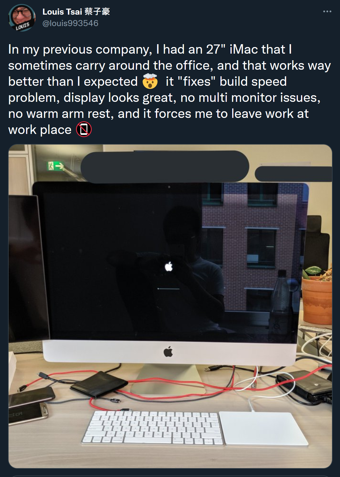 A screenshot of a Tweet from Louis (@louis993546), which has a picture of an iMac in the boot screen, on an office desk. The tweet writes "In my previous company, I had an 27" iMac that I sometimes carry around the office, and that works way better than I expected π€― it "fixes" build speed problem, display looks great, no multi monitor issues, no warm arm rest, and it forces me to leave work at work place π΅"